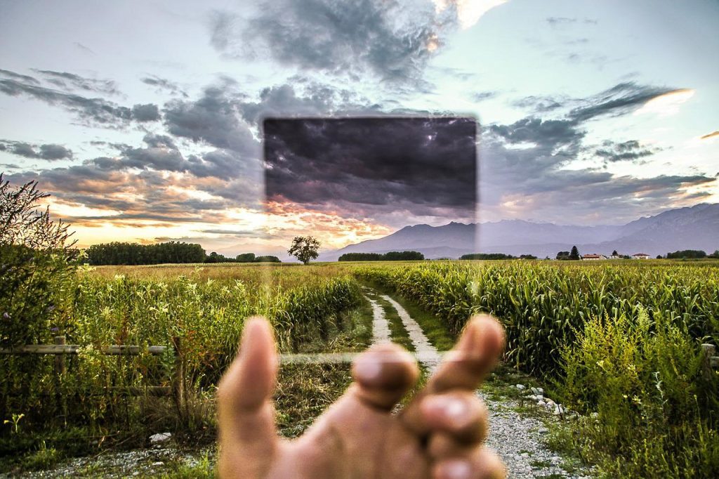 A square piece of glass being held up in front of a dirt road going through a field