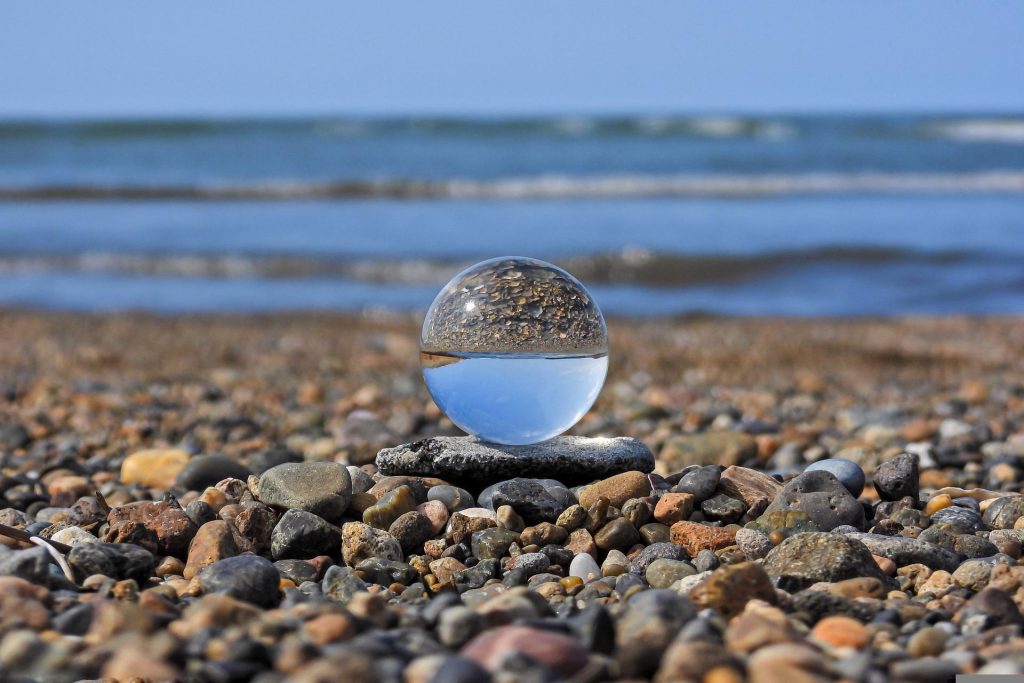 Glass sphere or lens ball sitting on a rocky shore with water in the background
