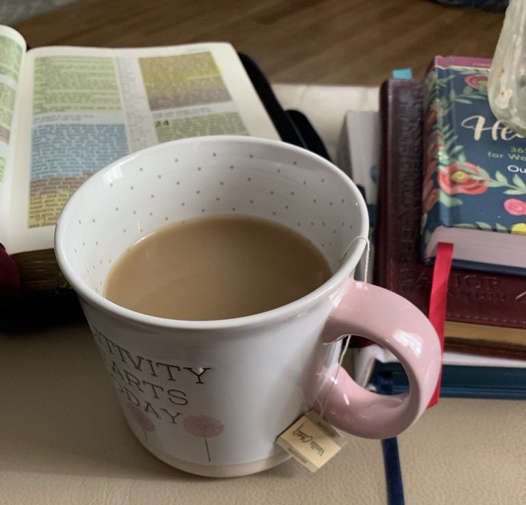 Mug filled with tea and sitting beside a Bible and devotionals.